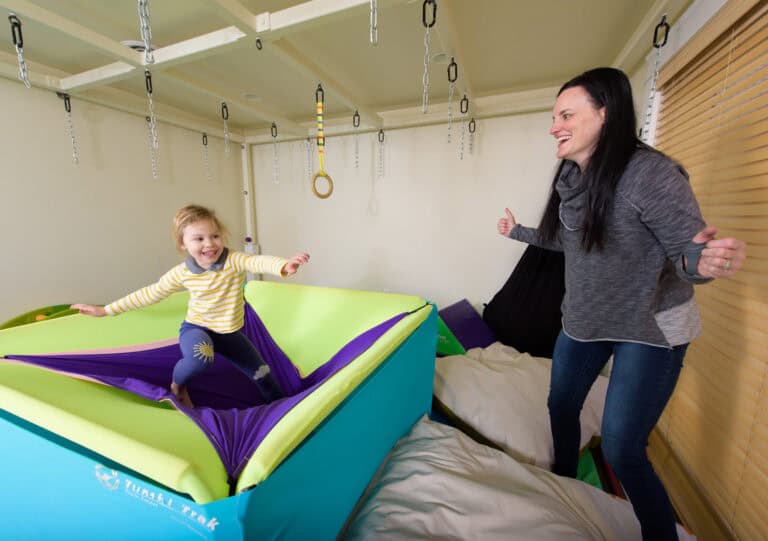 A photo of a therapist and young client doing a balance exercise on the Boundex Cuddle Box.