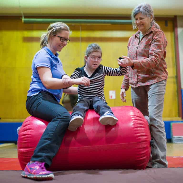 A pair of occupation therapists work with a client who sits on the air barrel.