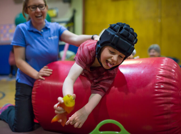 An occupation therapist works with a client who is lying across the air barrel.
