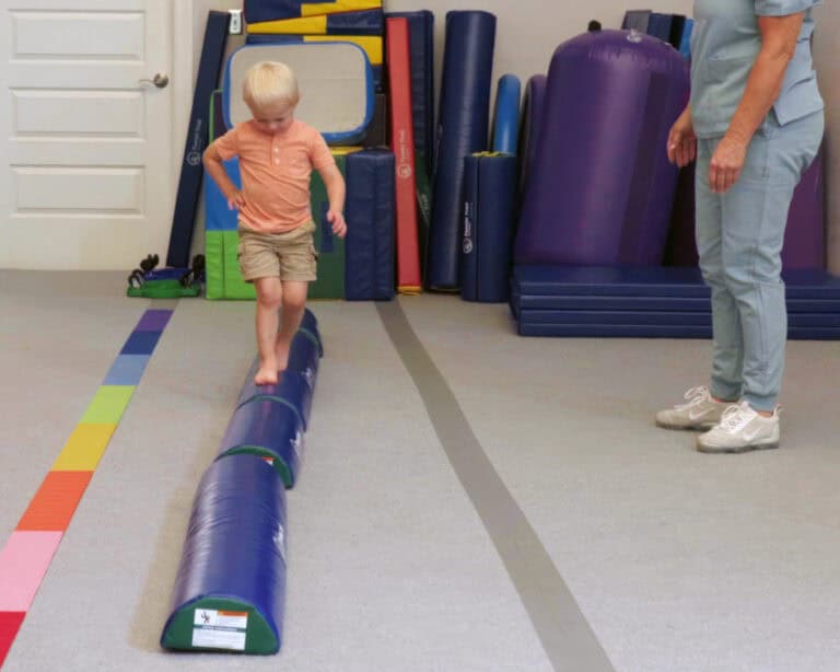 A child walks a line of Half Rounds while his therapist watches.