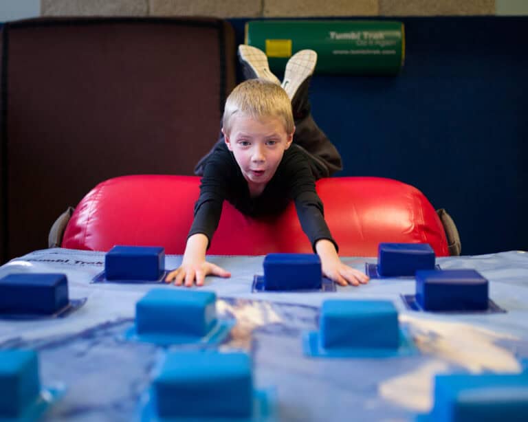 A photo of a boy with a wonderous expression on his face rolling off an Air Barrel onto a Climbing Wall Overlay.