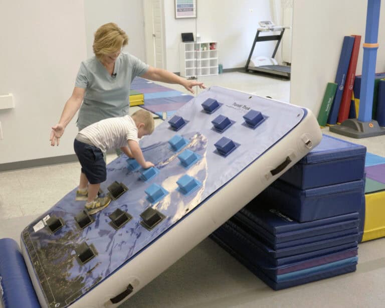 A photo of a therapist working with a young client who is on a Climbing Wall Overlay.