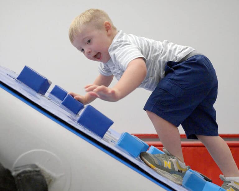 A photo of a boy with a happy expression on his face climbing a Climbing Wall Overlay.