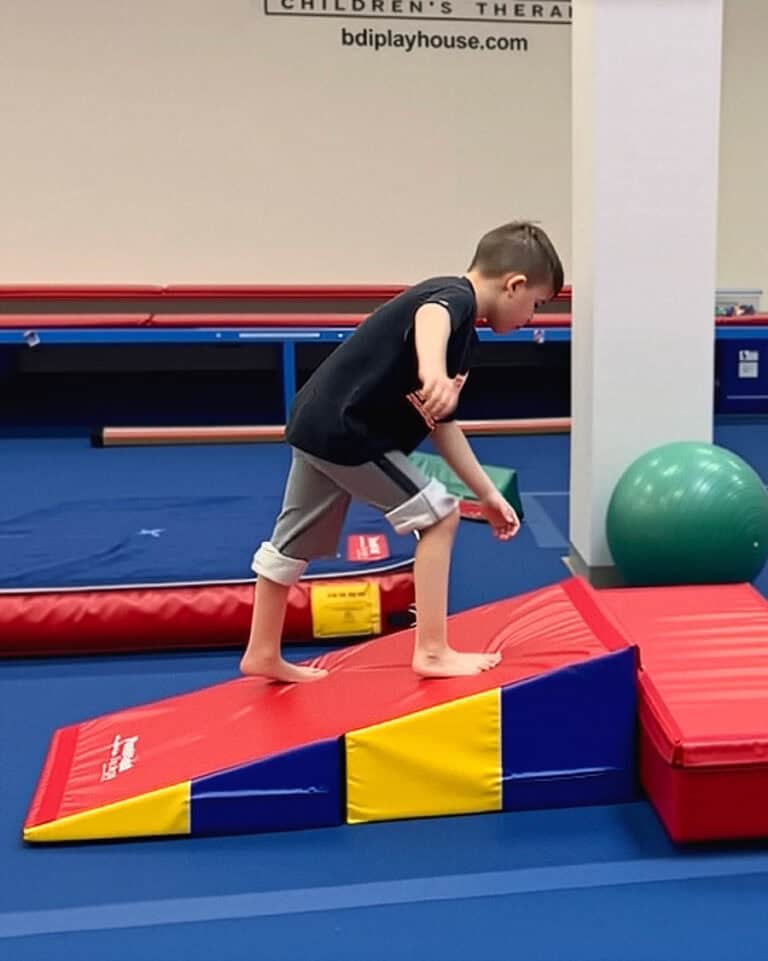 A photo of a boy in a therapy clinic walking up a Folding Incline Mat.