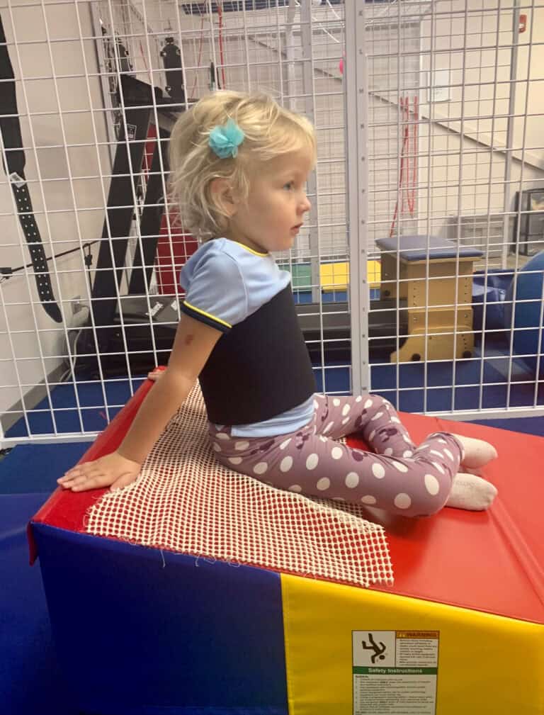 A photo of a girl in a therapy clinic sitting on a Folding Incline Mat.