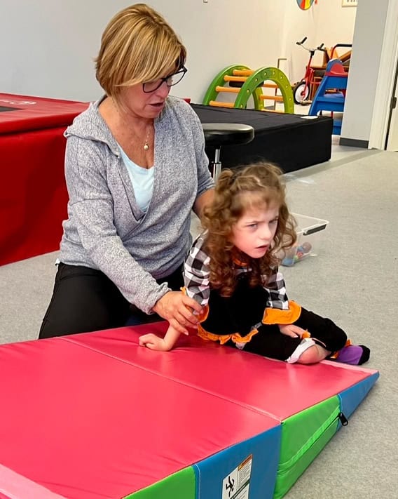 A photo of an occupational therapist and a girl in a therapy clinic working on a Folding Incline Mat.