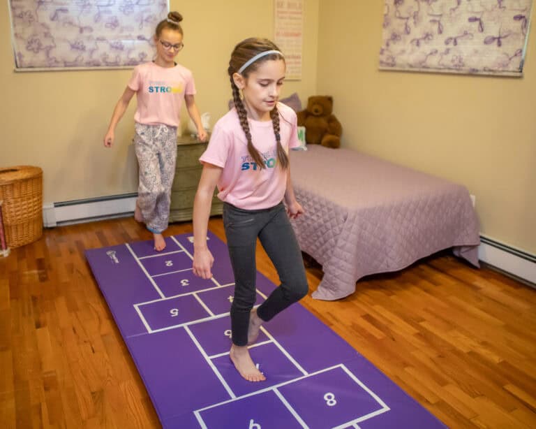 A photo of two girls playing hopscotch on a Hopscotch Mat.