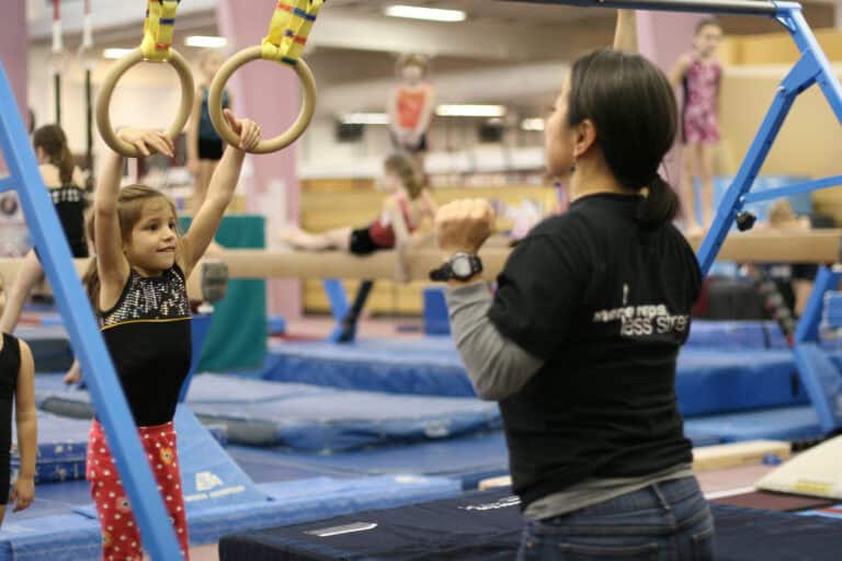 A photo of a client hanging from the Movement Rings, watched by a therapist.