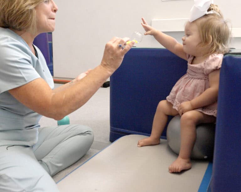 A photo of an occupational therapist working with a young client sitting against the back of the Tumbl Trak Steps.