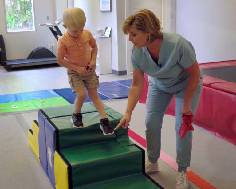 A photo of a boy walking on the top of two Tumbl Trak Steps joined back-to-back, assisted by an occupational therapist.