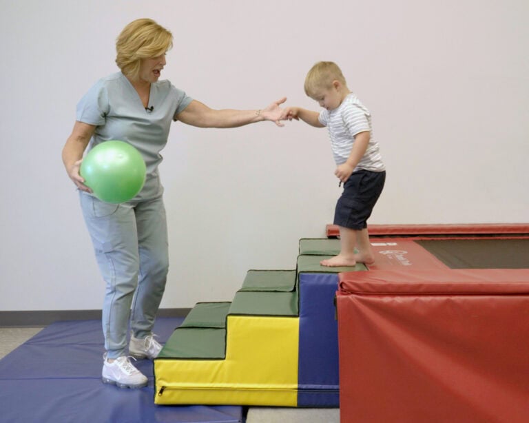 A photo of a therapist helping a boy walk down from the Tumbl Trak using Tumbl Trak Steps.