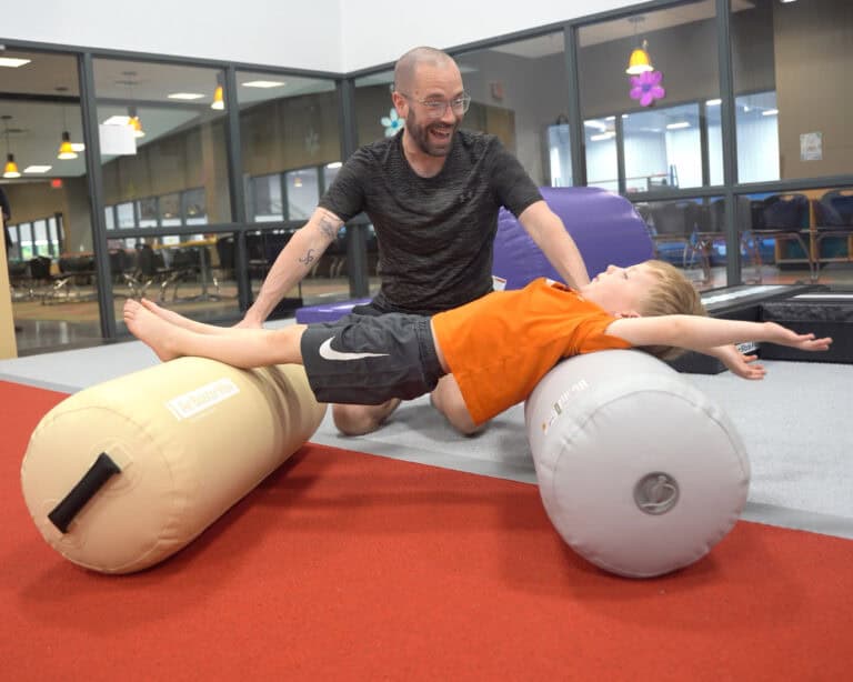 A photo of an occupational therapist working with a boy who is is stretching across two Air Bolster Minis.