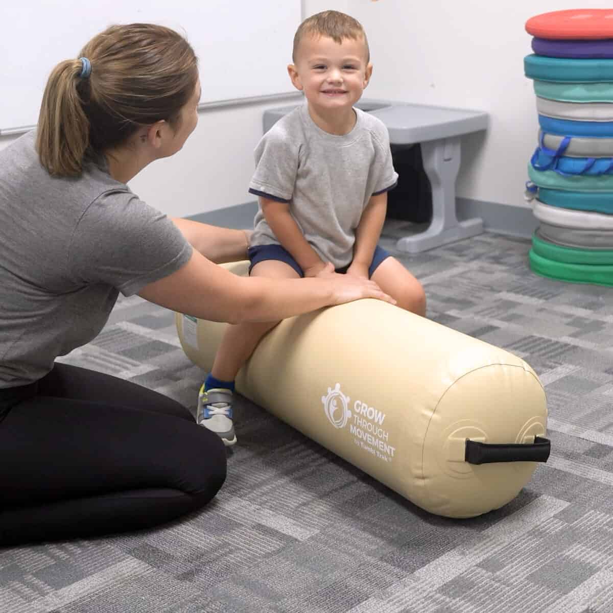 A boy sits on an Air Bolster Mini working with his occupational therapist.