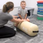A boy sits on an Air Bolster Mini working with his occupational therapist.