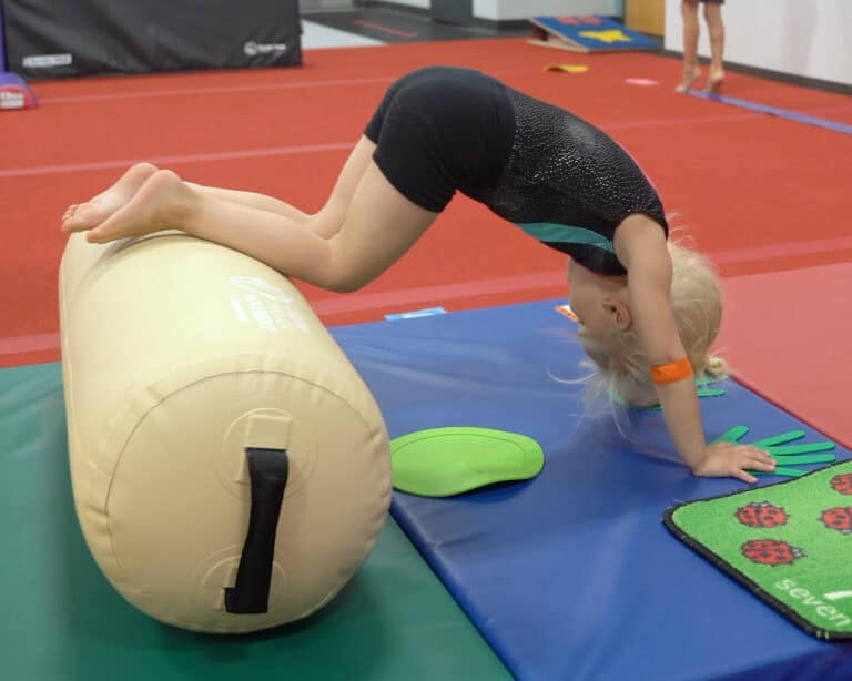 A photo of a girl using an Air Bolster Mini to do a pose onto a mat with nearby manipulatives.