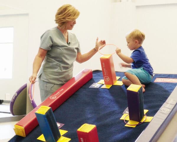 A photo of a pediatric occupational therapist working with a client on a Power Launch with Carpet Wall Overlay on top and with Fun Sticks.